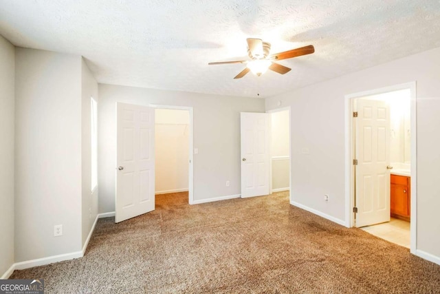 unfurnished bedroom featuring ensuite bath, a textured ceiling, light colored carpet, ceiling fan, and a spacious closet