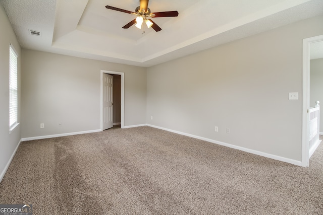 empty room featuring a raised ceiling, a wealth of natural light, carpet, and ceiling fan