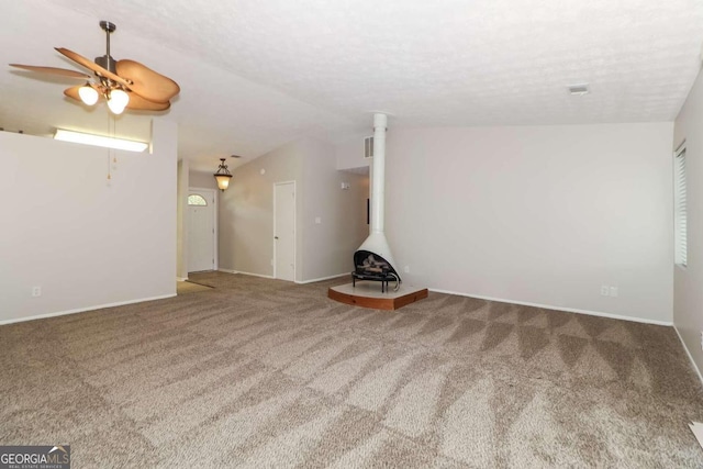 unfurnished living room featuring carpet flooring, a wood stove, ceiling fan, and a textured ceiling