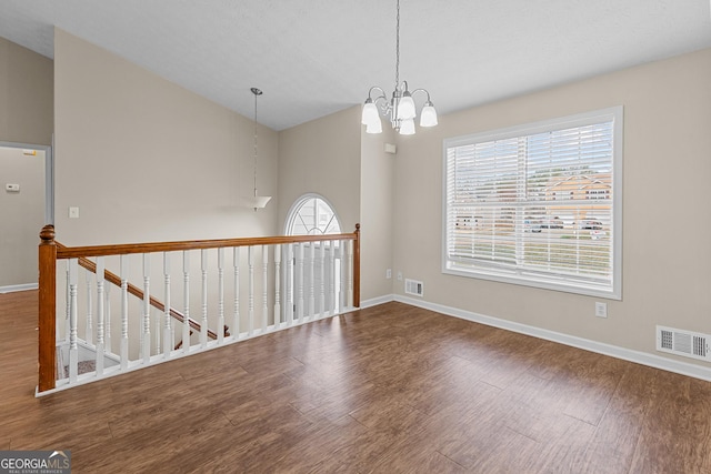 spare room with vaulted ceiling, hardwood / wood-style floors, and an inviting chandelier