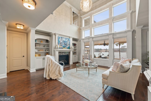 living room with built in features, dark wood-type flooring, a high end fireplace, and crown molding