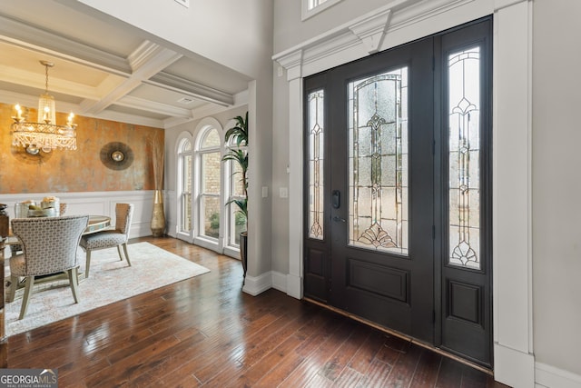 entrance foyer featuring beam ceiling, ornamental molding, coffered ceiling, dark wood-type flooring, and a chandelier