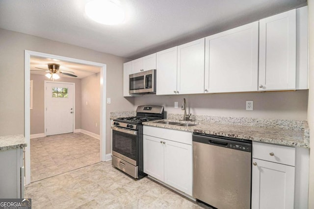 kitchen with white cabinets, stainless steel appliances, light stone counters, and sink