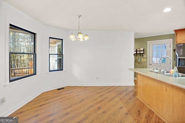 unfurnished dining area with light wood-type flooring, plenty of natural light, a notable chandelier, and sink