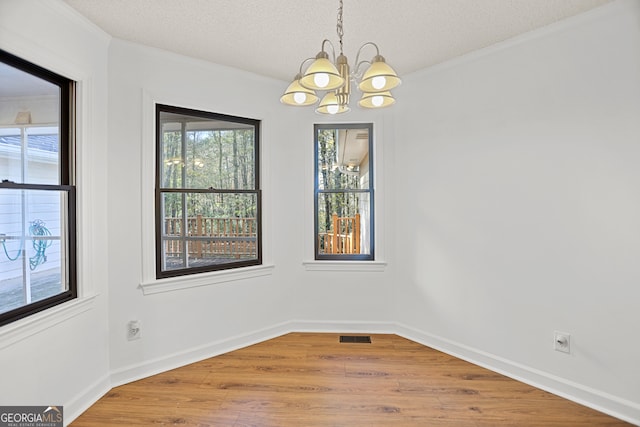 unfurnished dining area with crown molding, wood-type flooring, a textured ceiling, and an inviting chandelier