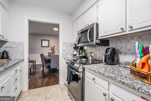 kitchen with black range with electric stovetop, light stone counters, light hardwood / wood-style flooring, and white cabinets