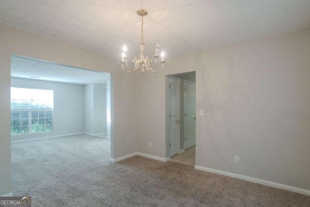 unfurnished room featuring light carpet, a textured ceiling, and a notable chandelier