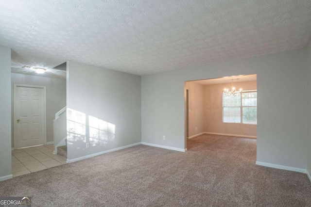 carpeted spare room featuring a textured ceiling and an inviting chandelier