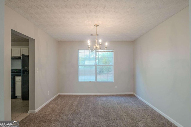 carpeted empty room featuring a textured ceiling and a chandelier