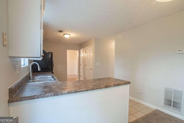 kitchen featuring sink, light tile patterned floors, refrigerator, a textured ceiling, and white cabinets