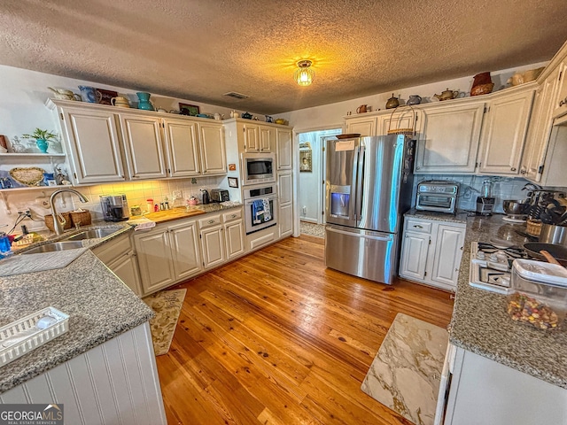 kitchen featuring sink, a textured ceiling, decorative backsplash, appliances with stainless steel finishes, and light wood-type flooring