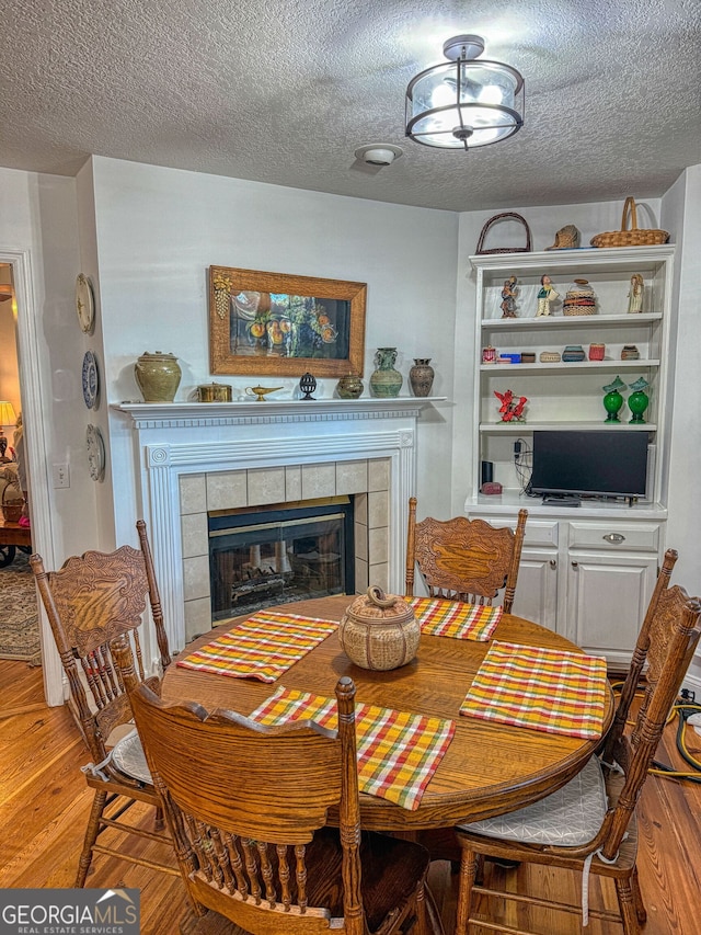 dining space with a tile fireplace, hardwood / wood-style floors, and a textured ceiling