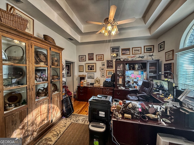 office featuring a raised ceiling, ceiling fan, and light hardwood / wood-style flooring