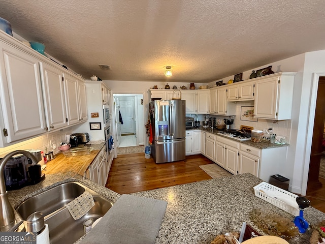 kitchen featuring sink, dark hardwood / wood-style flooring, backsplash, a textured ceiling, and appliances with stainless steel finishes