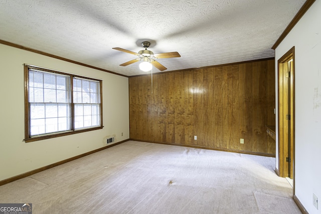 unfurnished room featuring ceiling fan, wood walls, ornamental molding, and a textured ceiling