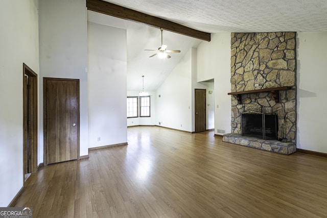 unfurnished living room featuring hardwood / wood-style floors, a stone fireplace, ceiling fan, a textured ceiling, and beamed ceiling