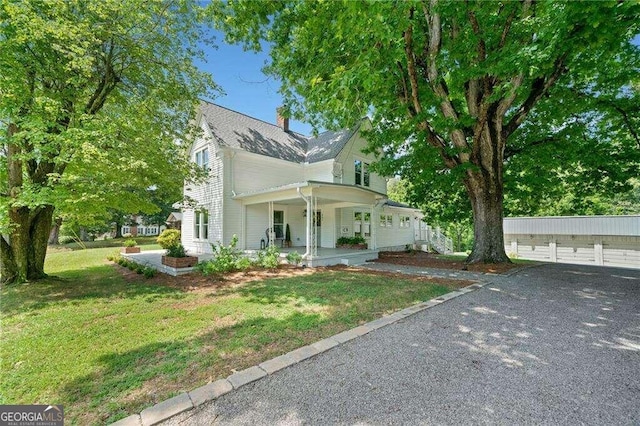 view of front of house with covered porch, a garage, an outdoor structure, and a front yard