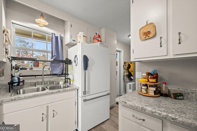 kitchen with white cabinetry, sink, white fridge, light hardwood / wood-style floors, and a textured ceiling