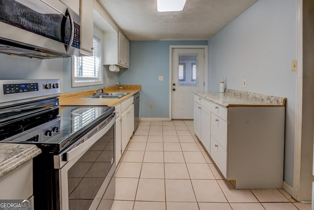 kitchen with light tile patterned flooring, appliances with stainless steel finishes, sink, and white cabinets