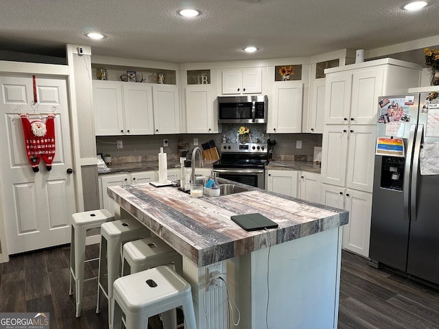 kitchen with a kitchen breakfast bar, a textured ceiling, stainless steel appliances, a kitchen island with sink, and white cabinetry