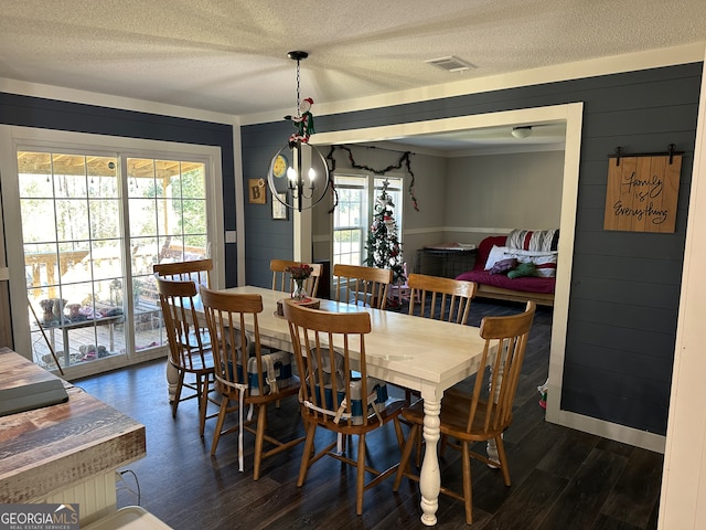 dining space featuring a textured ceiling, dark hardwood / wood-style flooring, wooden walls, and a notable chandelier