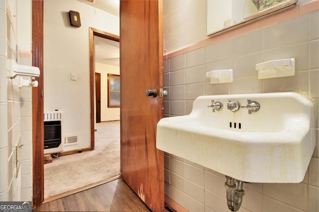 bathroom with heating unit, hardwood / wood-style floors, tile walls, and sink