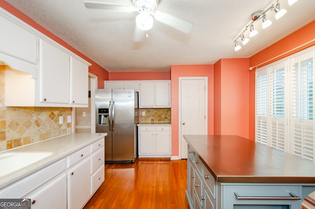 kitchen featuring backsplash, ceiling fan, stainless steel fridge, light wood-type flooring, and white cabinetry