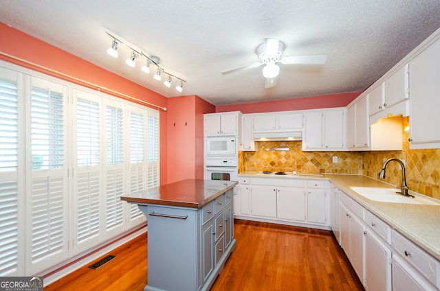 kitchen with white appliances, sink, white cabinets, hardwood / wood-style floors, and a center island