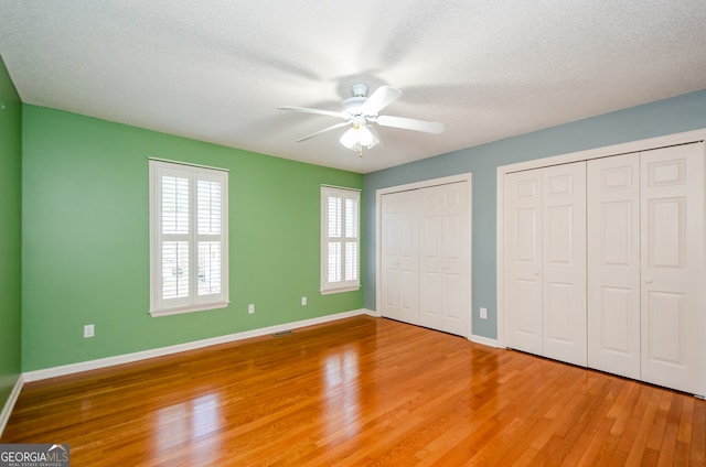 unfurnished bedroom with hardwood / wood-style floors, a textured ceiling, two closets, and ceiling fan