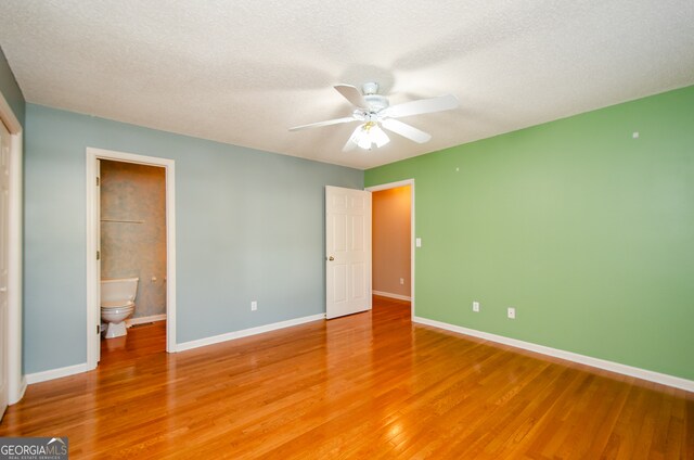 unfurnished bedroom featuring ensuite bathroom, ceiling fan, wood-type flooring, and a textured ceiling