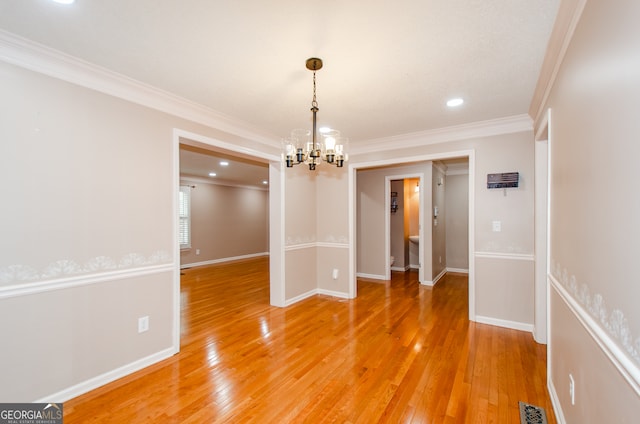 unfurnished dining area featuring ornamental molding, wood-type flooring, and an inviting chandelier