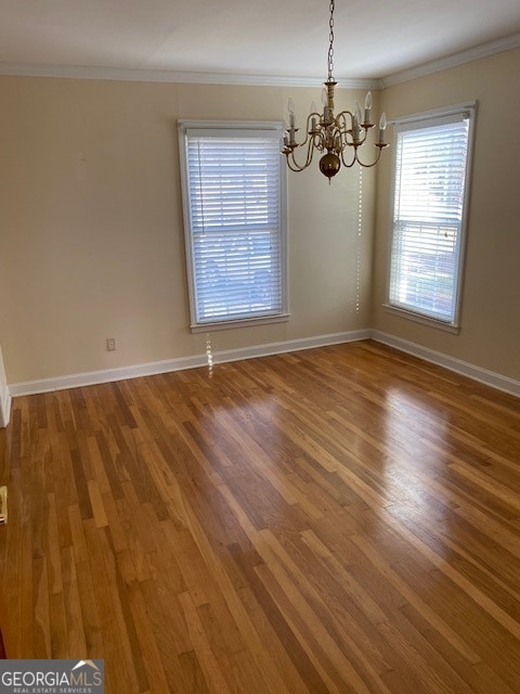 spare room with hardwood / wood-style flooring, crown molding, and a notable chandelier