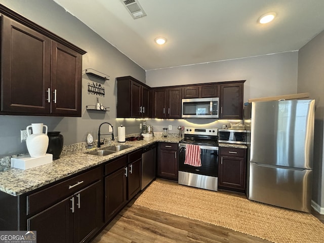 kitchen featuring stainless steel appliances, sink, light wood-type flooring, dark brown cabinetry, and light stone countertops