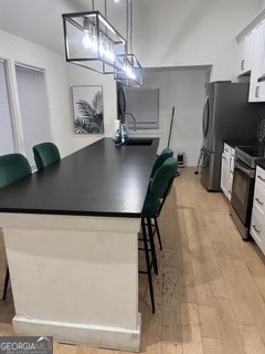 kitchen with a kitchen breakfast bar, appliances with stainless steel finishes, decorative light fixtures, light hardwood / wood-style floors, and white cabinetry