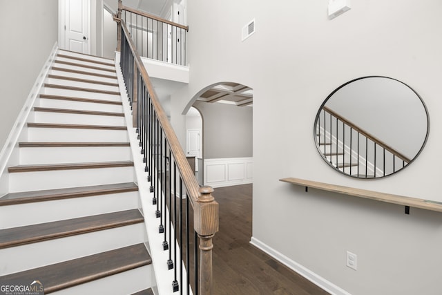 stairway with a towering ceiling, coffered ceiling, and hardwood / wood-style flooring