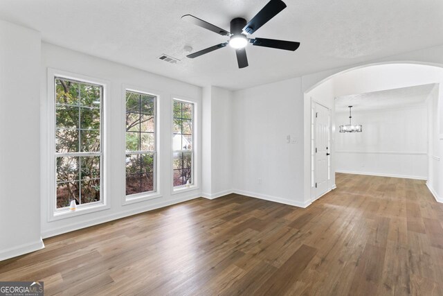 empty room with hardwood / wood-style floors, ceiling fan with notable chandelier, and a textured ceiling