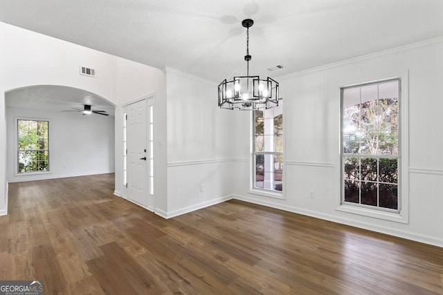 unfurnished dining area with ceiling fan with notable chandelier, crown molding, and dark wood-type flooring