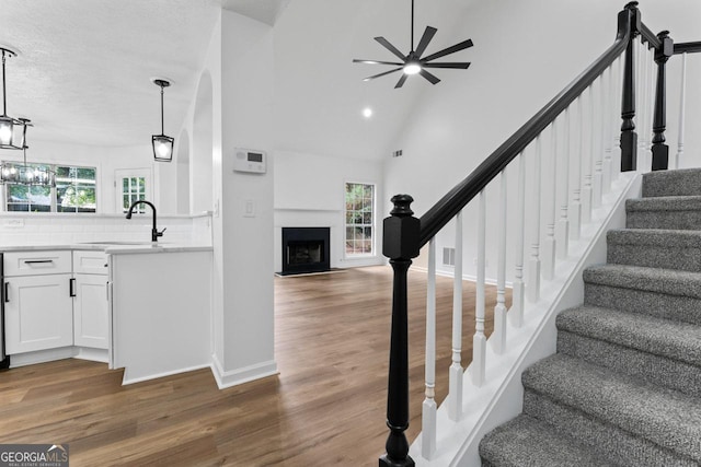 staircase featuring ceiling fan, sink, high vaulted ceiling, wood-type flooring, and a textured ceiling