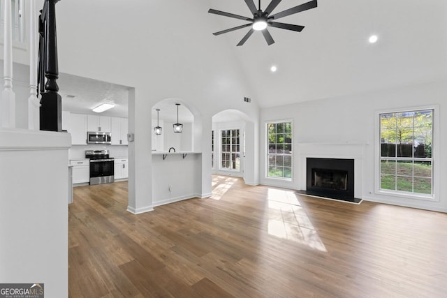 unfurnished living room featuring wood-type flooring, high vaulted ceiling, and ceiling fan