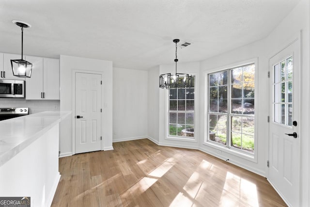 unfurnished dining area with a chandelier, light hardwood / wood-style floors, and a textured ceiling