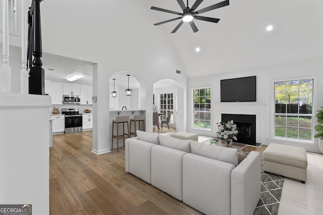 living room featuring ceiling fan, high vaulted ceiling, and light wood-type flooring