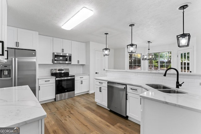 kitchen with light wood-type flooring, stainless steel appliances, sink, decorative light fixtures, and white cabinetry