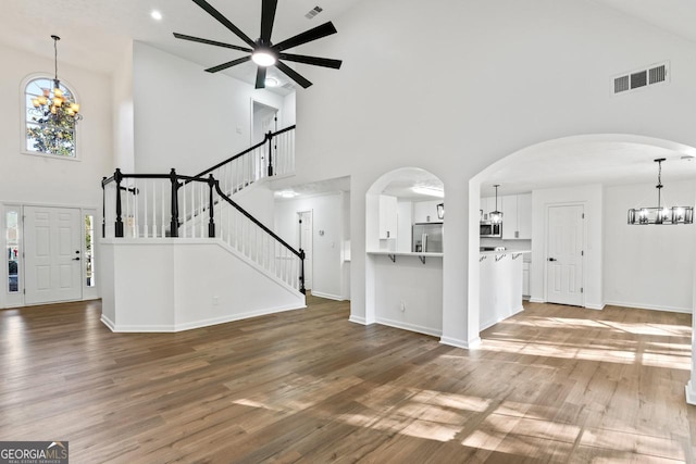 unfurnished living room featuring high vaulted ceiling, wood-type flooring, and ceiling fan with notable chandelier