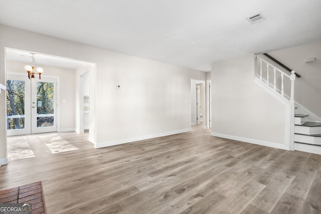 unfurnished living room with a notable chandelier, french doors, and light hardwood / wood-style flooring