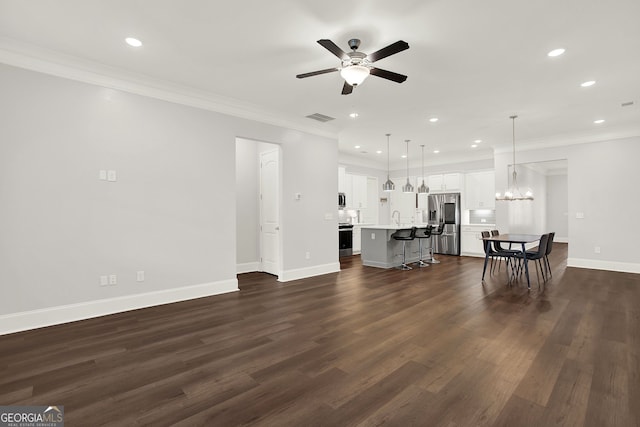 unfurnished living room featuring ceiling fan with notable chandelier, dark hardwood / wood-style floors, and crown molding