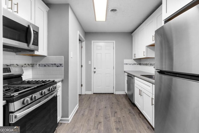 kitchen featuring light wood-type flooring, white cabinetry, appliances with stainless steel finishes, and tasteful backsplash