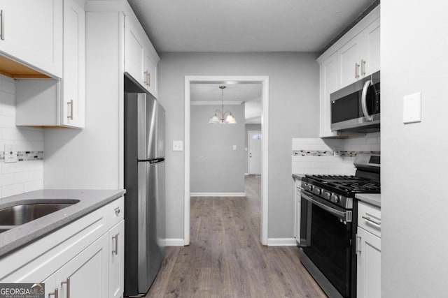 kitchen featuring an inviting chandelier, light hardwood / wood-style flooring, decorative backsplash, appliances with stainless steel finishes, and white cabinetry