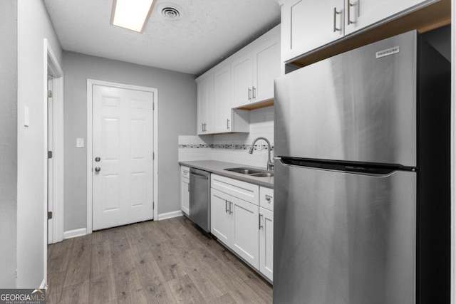 kitchen featuring backsplash, white cabinets, sink, light hardwood / wood-style floors, and stainless steel appliances