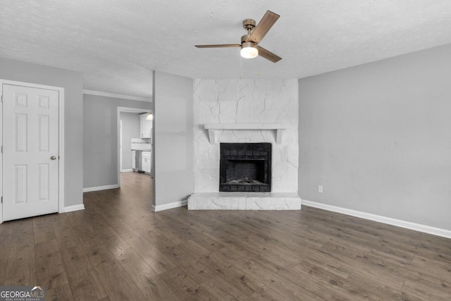 unfurnished living room featuring a textured ceiling, a stone fireplace, ceiling fan, and dark wood-type flooring