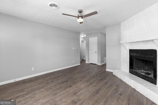 unfurnished living room with a stone fireplace, ceiling fan, dark wood-type flooring, and a textured ceiling